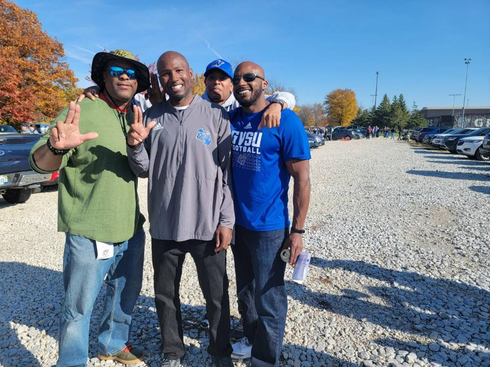 Four alumni show the Anchor Up sign during the tailgate.